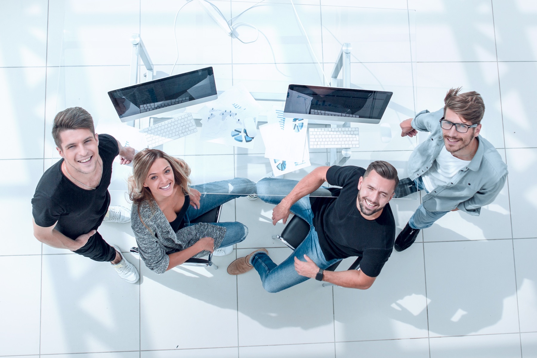 Équipe souriante autour d'un bureau équipé d'ordinateurs, vue de dessus